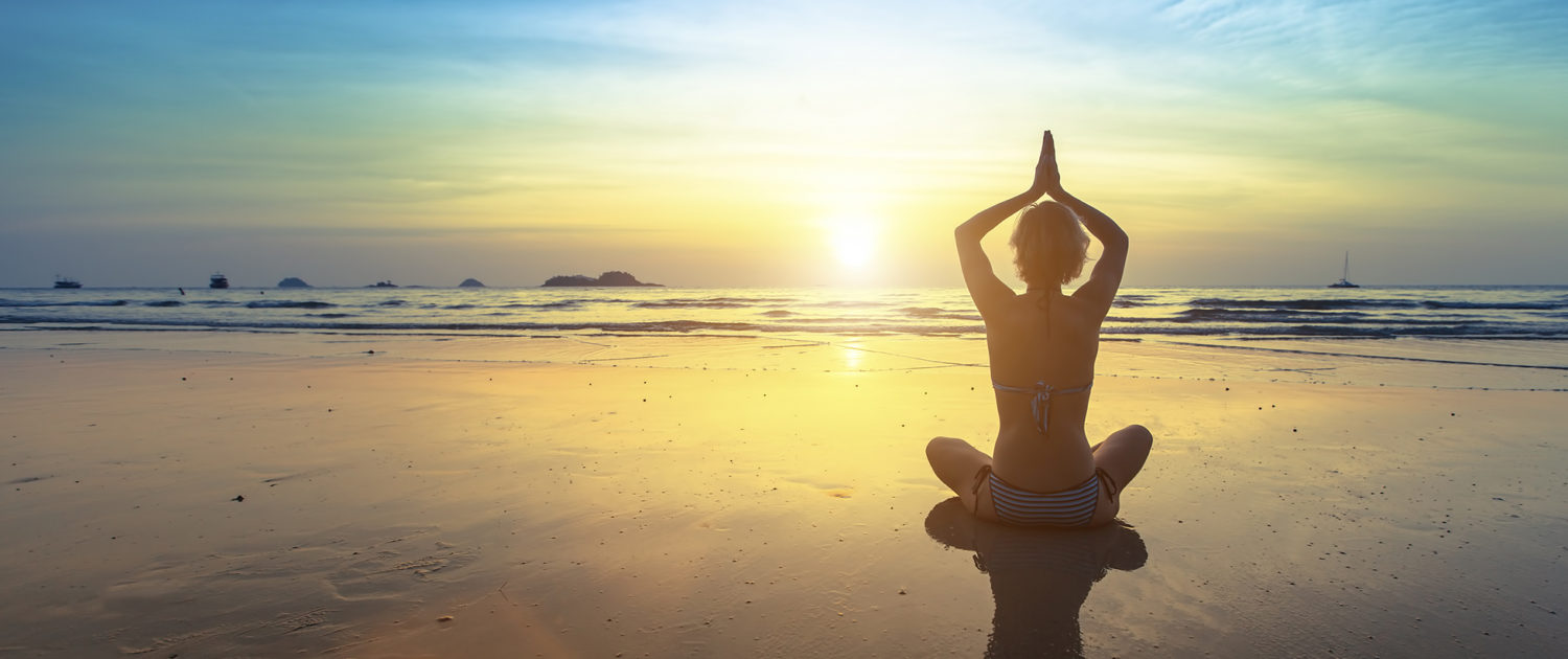 Yoga silhouette. Yoga woman sitting in lotus pose on the beach with reflection during sunset.